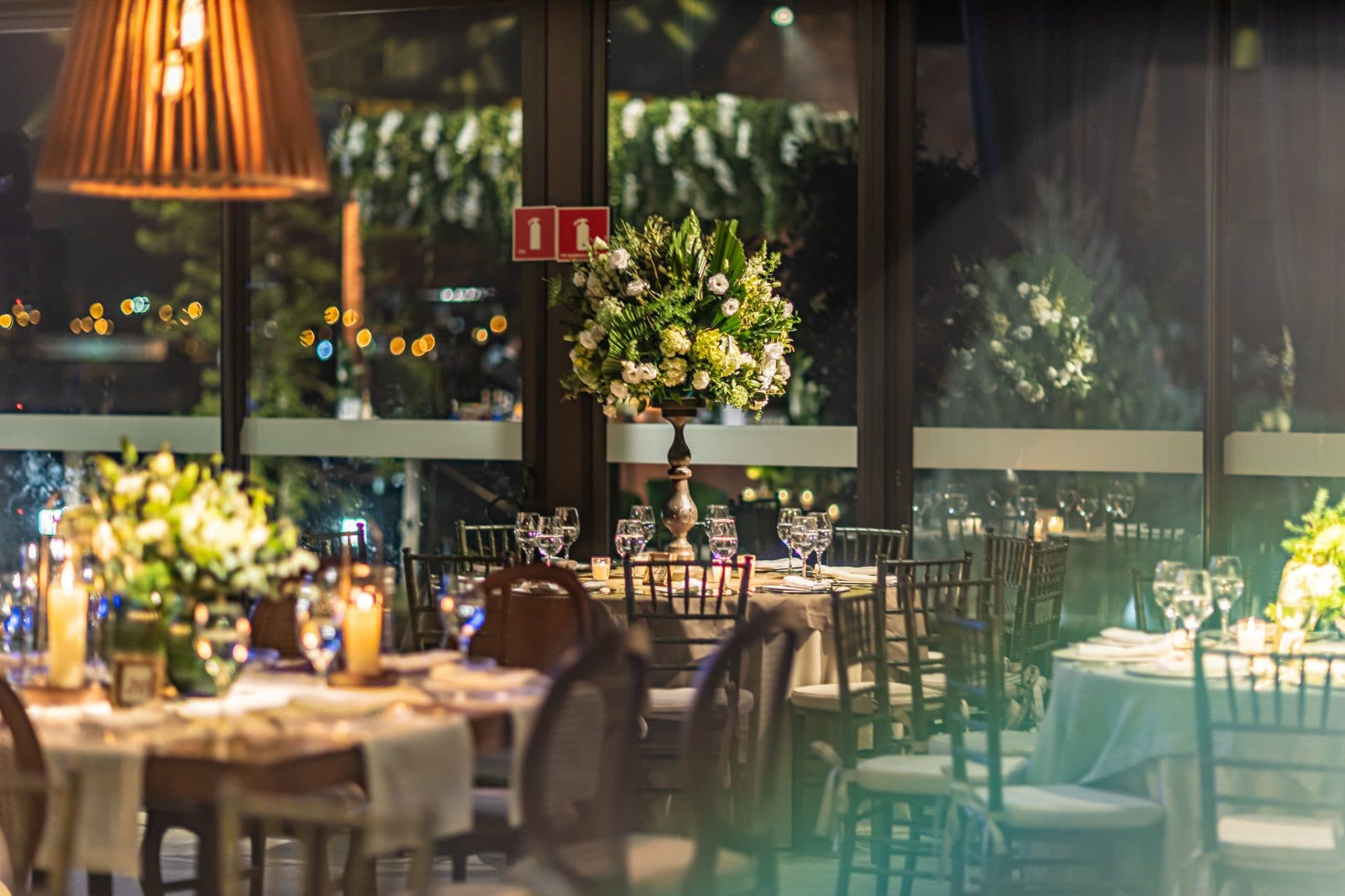 salón de evento con mesas redondas, sillas tiffany y centros de mesa florales altos